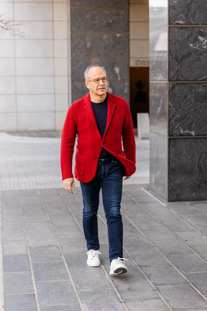 Ahmet Bozer walking in front of a modern business office wearing a red jacket, black t-shirt, and jeans in Buckhead Atlanta