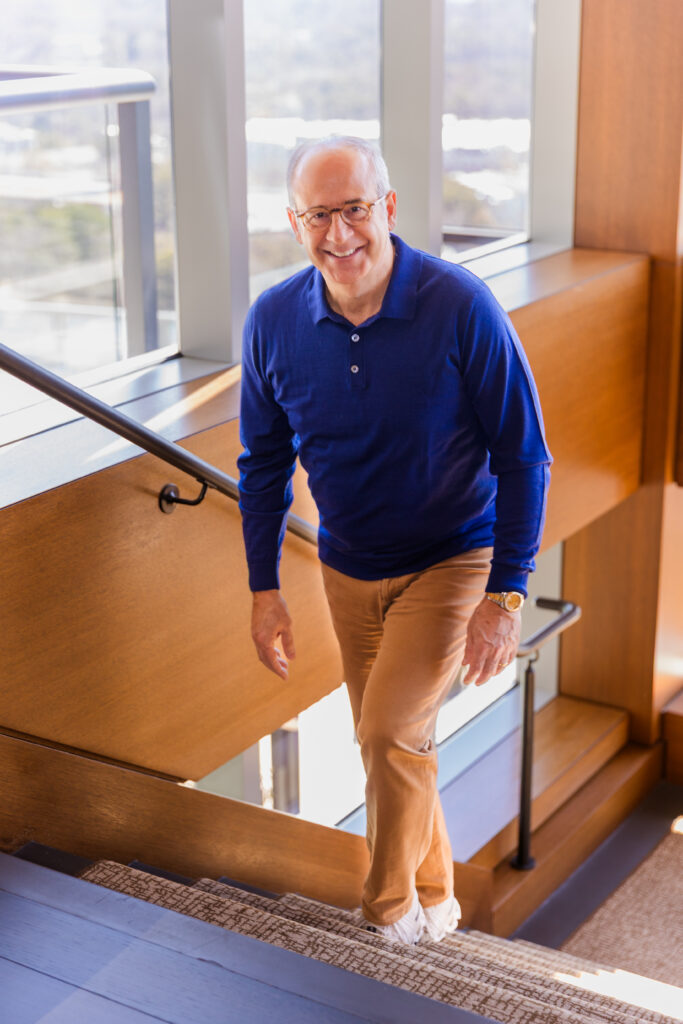 Ahmet Bozer walking upstairs surrounded by big windows, wearing a blue top and beige pants, during his Buckhead Atlanta personal brand session
