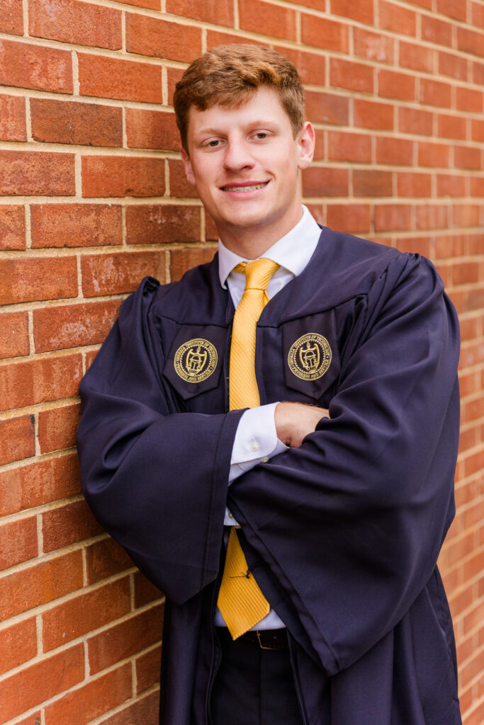 Jason leaning with arms crossed against a red brick wall on Georgia Tech campus.