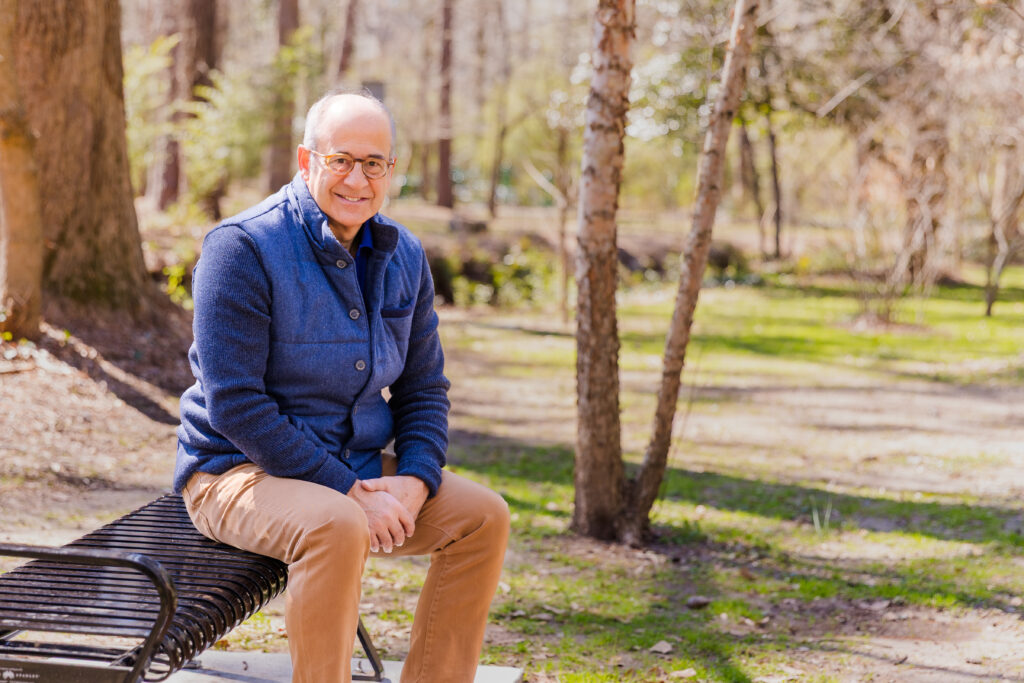 Ahmet Bozer wearing a sleeveless jacket and beige pants, sitting on a park bench, hands together, during his personal branding session in Buckhead