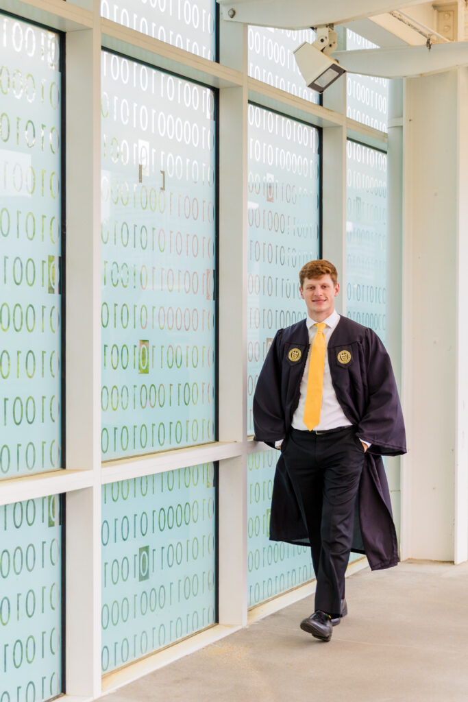 Wide shot of Jason walking along the transparent binary code wall on campus.
