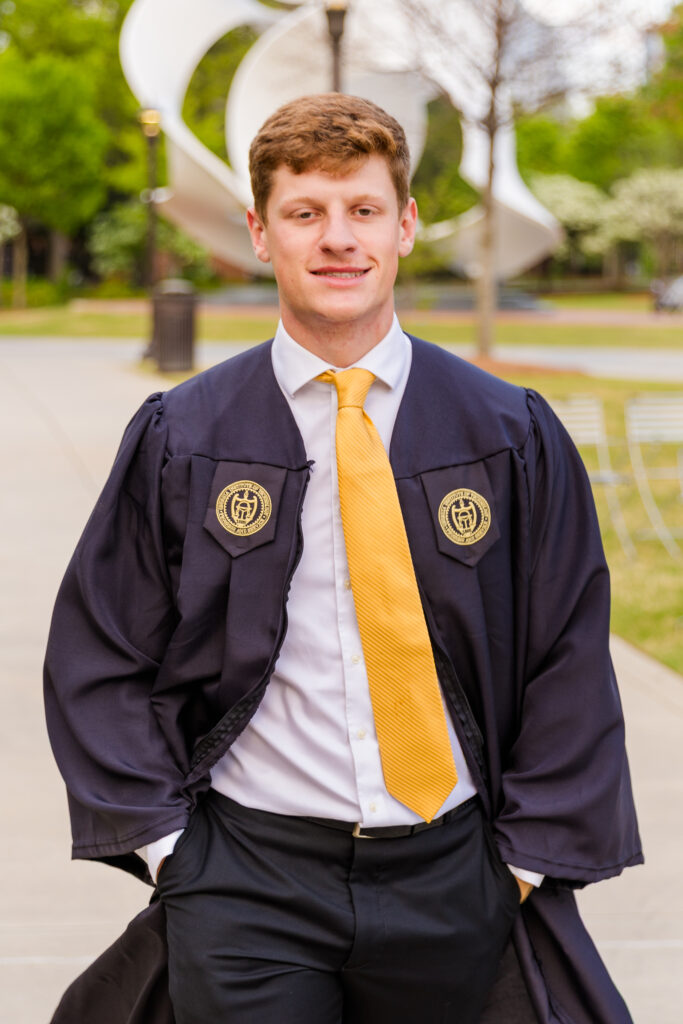 senior student Jason walking through Georgia Tech campus in graduation cap and gown.