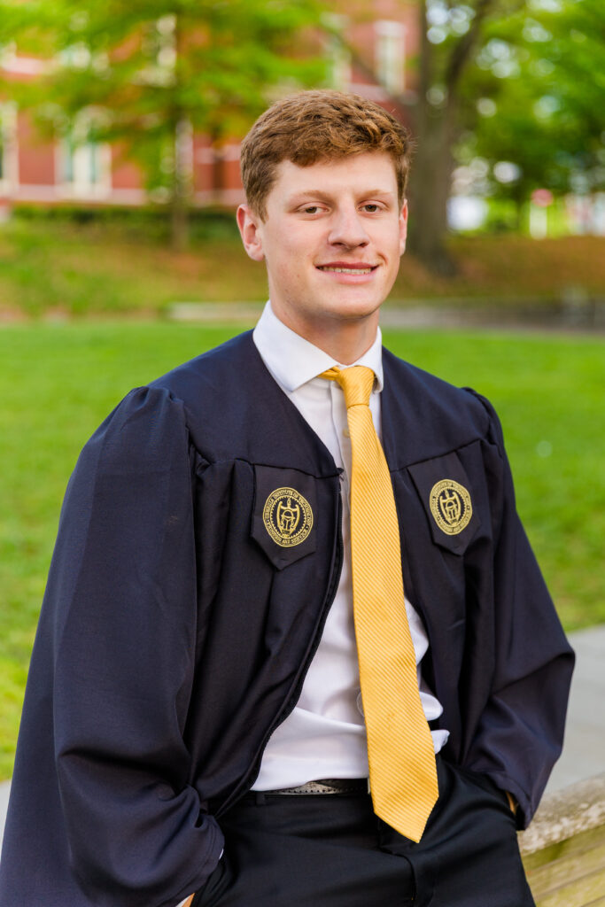 Close-up of Jason leaning against the back of a bench on campus, wearing his cap and gown.