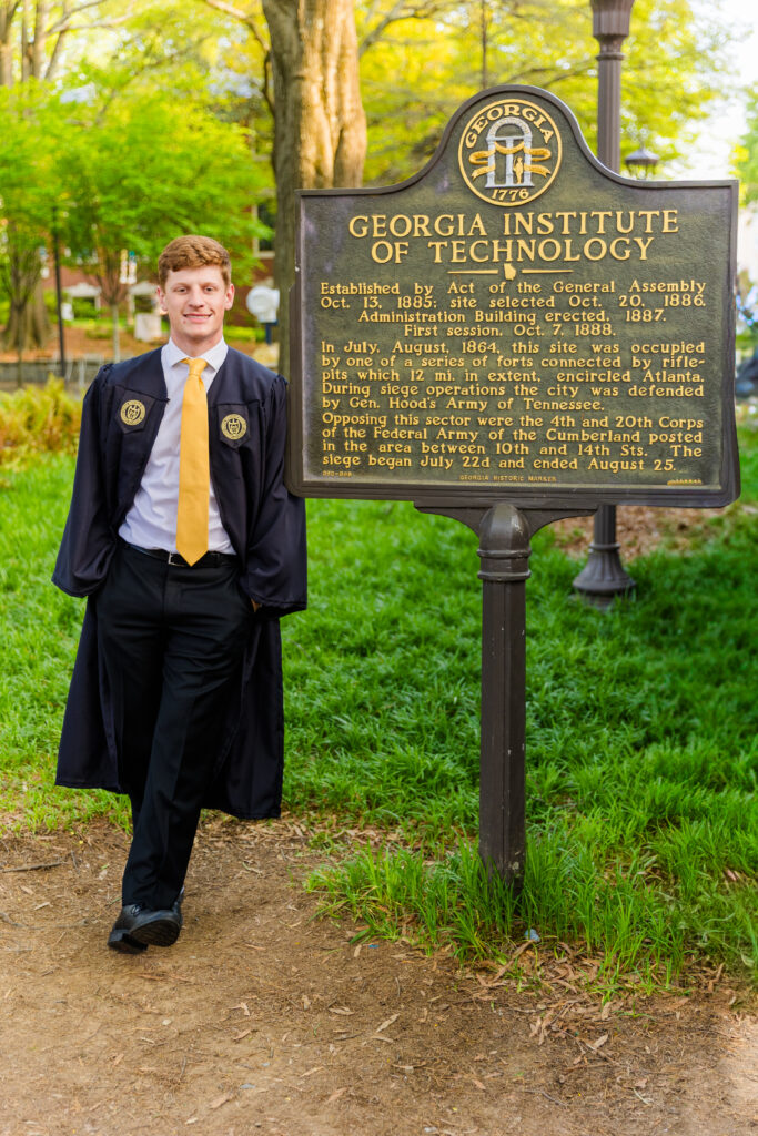 Jason senior standing by the Georgia Tech history sign in cap and gown.