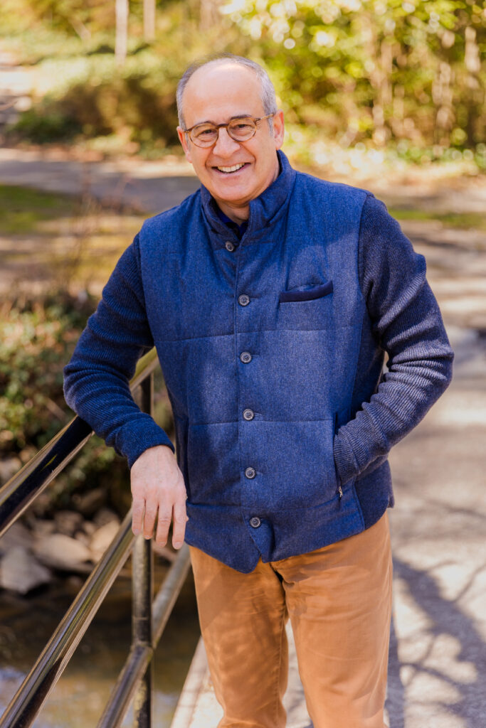 Ahmet Bozer standing on a bridge, hand resting on the handrail, wearing a sleeveless jacket during his outdoor personal brand session in Buckhead Atlanta