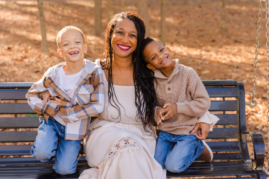 Mother sitting with her twin sons on a swing, all laughing during a candid family photo session in an Atlanta park by Laure Photography.