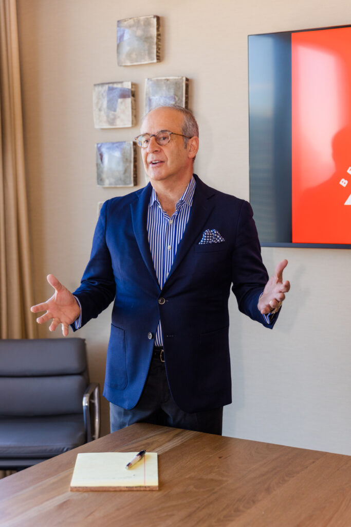 Ahmet Bozer presenting with hand gestures during a meeting in a conference room in Atlanta Buckhead, wearing a formal outfit