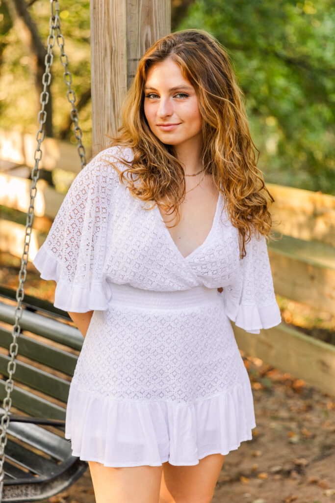 High school senior girl leaning playfully against a swing pole with hands behind her back during golden hour in Atlanta