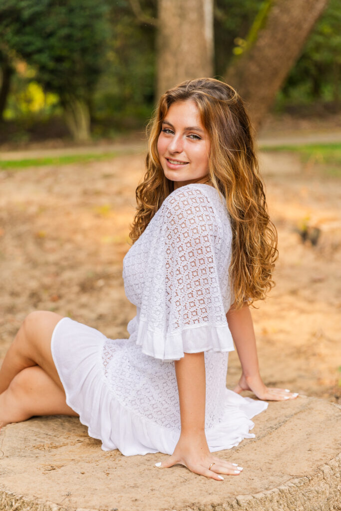 Senior girl sitting with crossed legs, leaning on hands, looking over her shoulder with soft expression during Atlanta session