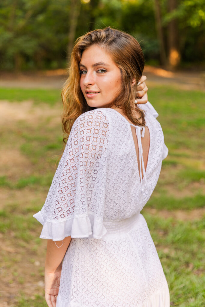 Curly-haired senior glancing over her shoulder with one hand in her hair during golden hour photos in an Atlanta park