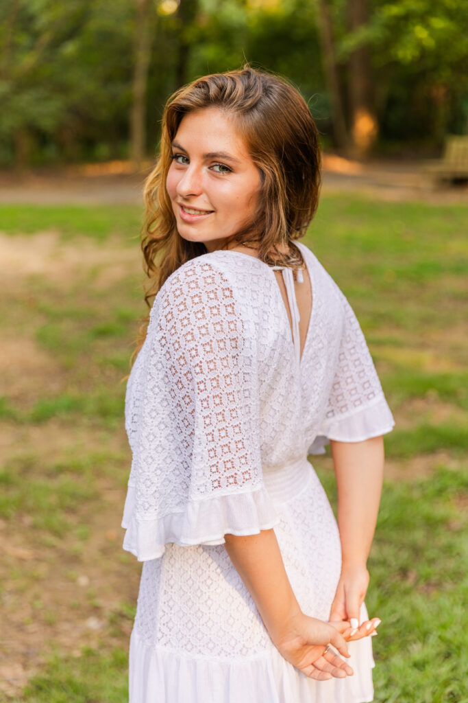 High school senior girl looking over her shoulder with hands clasped behind her back during golden hour in an Atlanta park