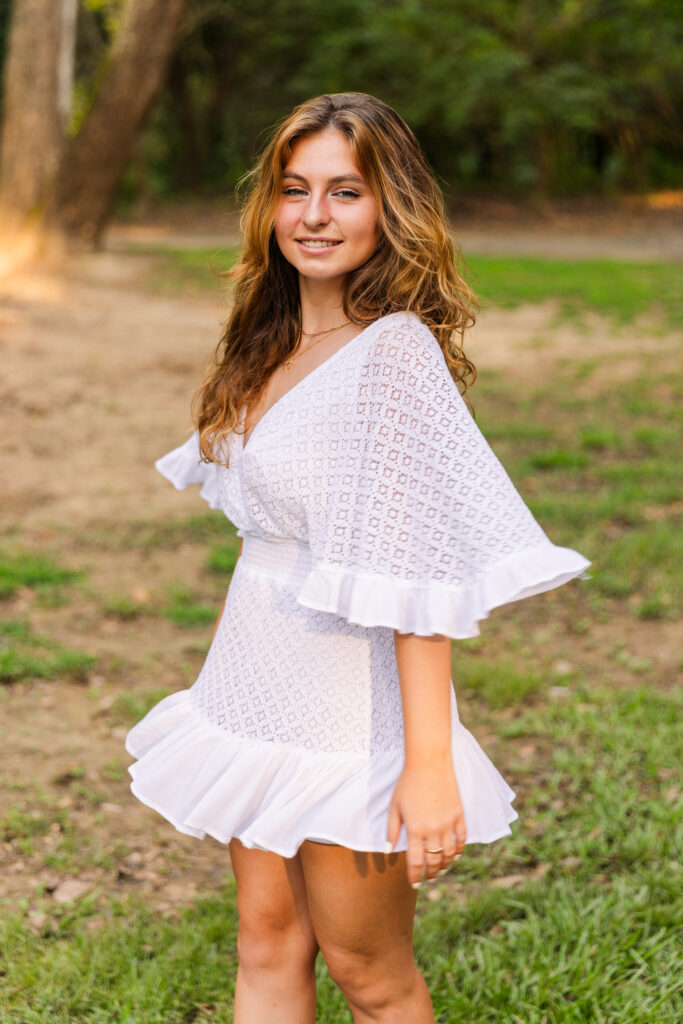 Side profile of high school senior spinning in a white textured dress in the park during golden hour