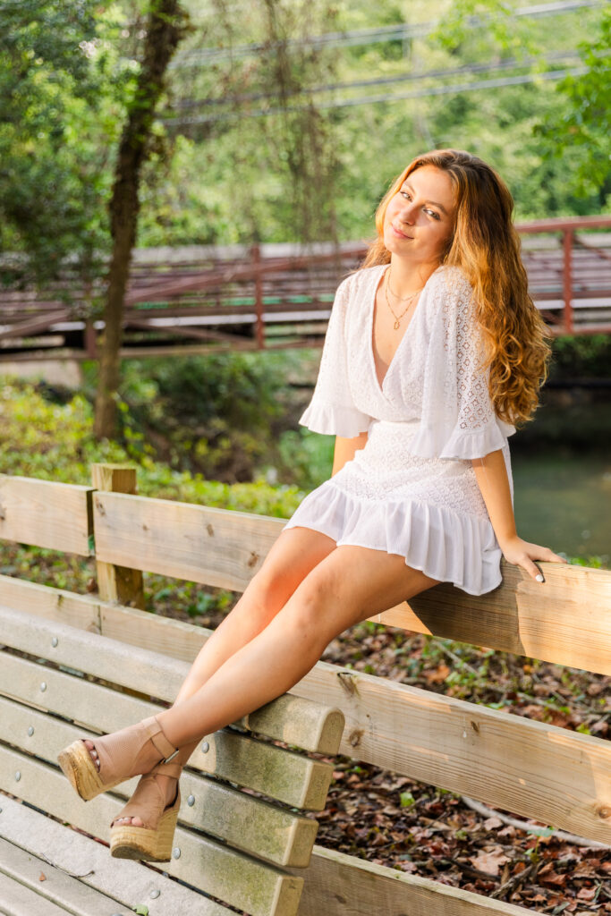 Sienna sitting on a wooden fence with ankles crossed and hands on each side during golden hour senior photos in Atlanta
