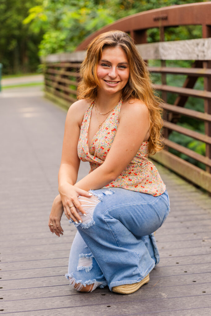 High school senior girl doing a sassy pose with one knee down on a bridge during her golden hour session in Atlanta