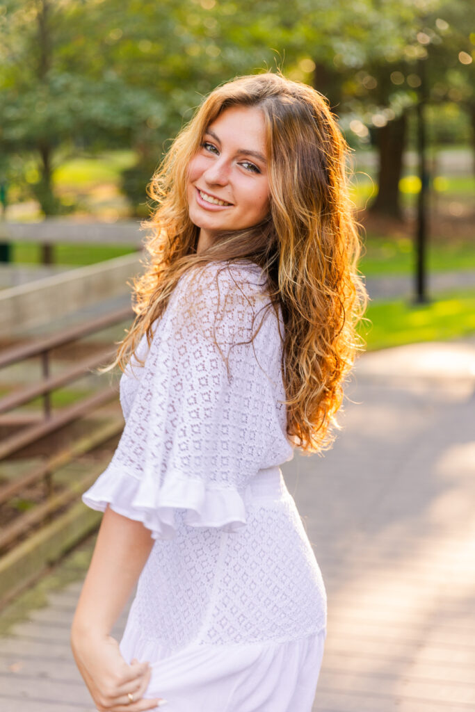 Senior girl in white textured dress looking over her shoulder during golden hour in an Atlanta park captured by Laure Photography