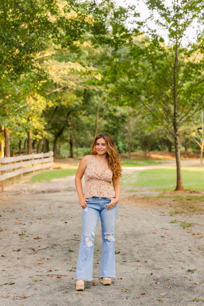 Senior girl standing in the middle of an Atlanta park path wearing jeans and a sleeveless floral top during summer session