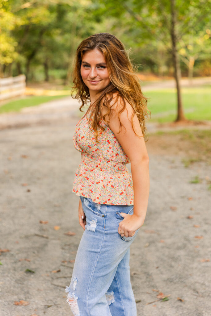 Senior girl with hand in back pocket looking over her shoulder, standing on a tree-lined path in an Atlanta park