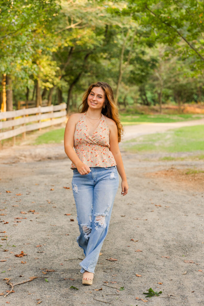 Wide-angle photo of senior girl walking toward the camera on a tree-lined path in Atlanta during golden hour