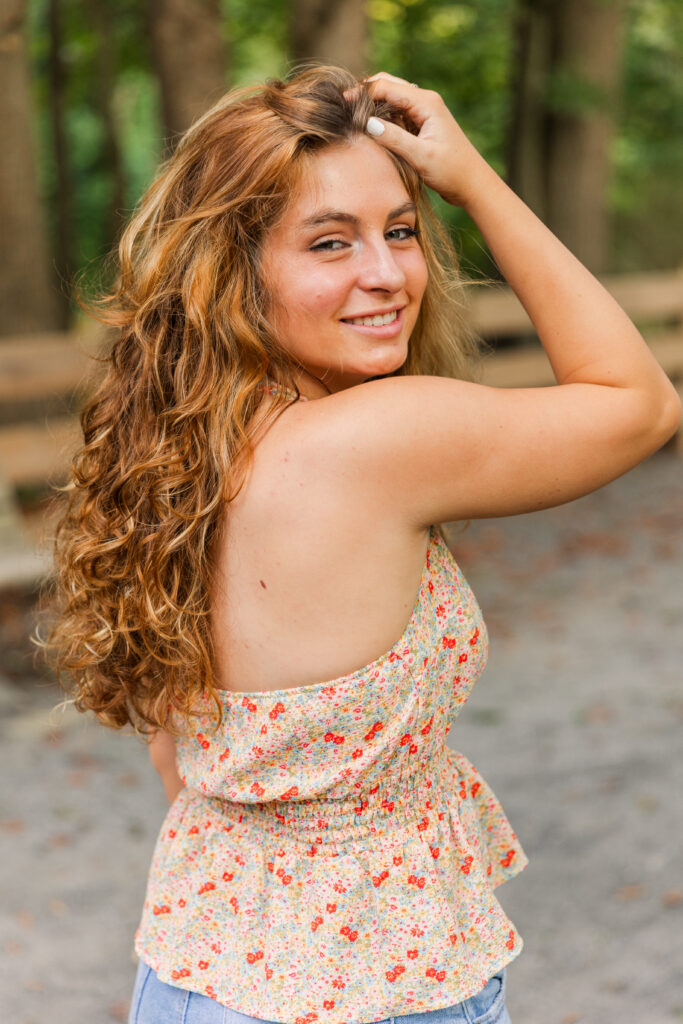 Close-up headshot of senior girl looking over her shoulder with hand in her hair, glowing in golden hour light
