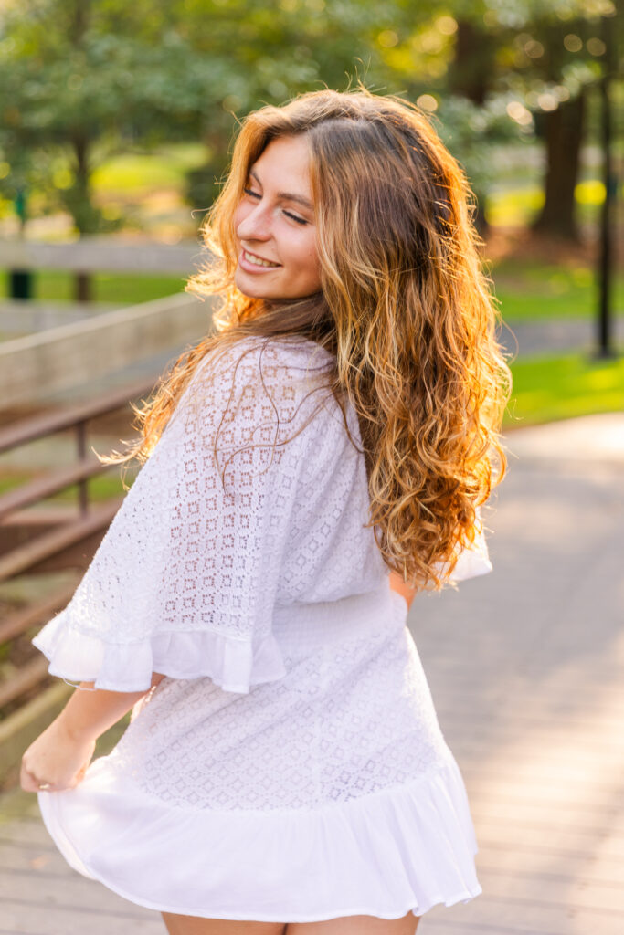 Senior girl spinning joyfully in a white dress on a wooden bridge during golden hour in an Atlanta park by Laure Photography