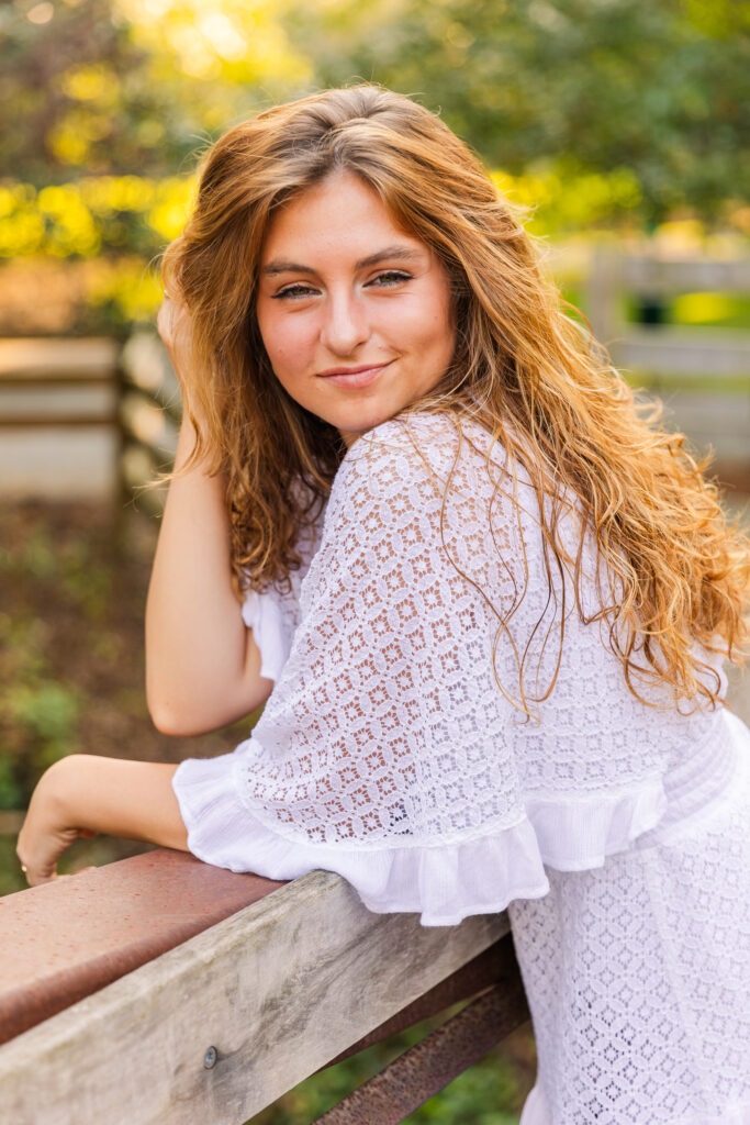 Graduate girl with curly hair leaning on bridge handrail, hand in hair, enjoying golden hour light in Atlanta park