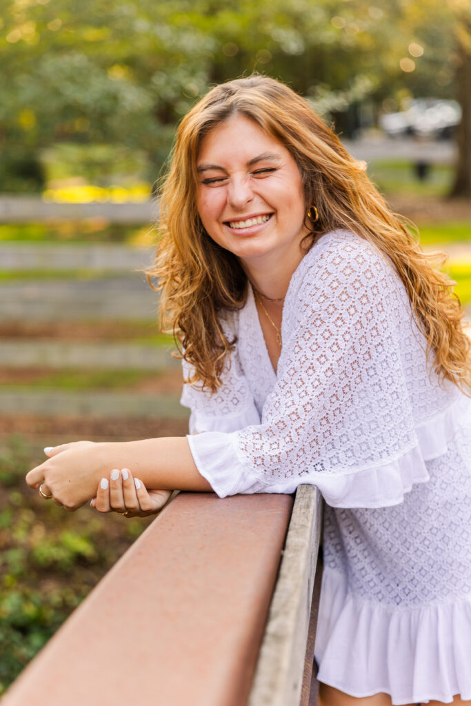 Senior girl resting her elbows on a wooden bridge handrail, glancing sideways at the camera in Atlanta park