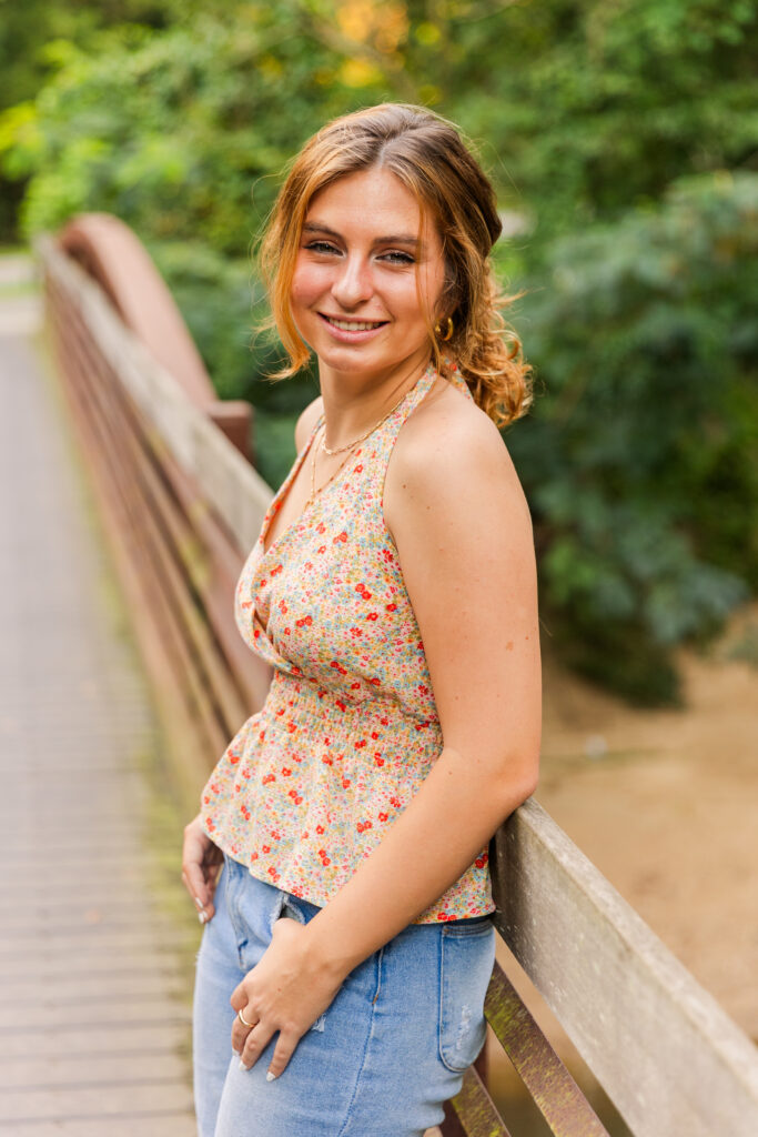 high school girl searing summer sleeveless flowery top and jeans leaning against a bridge in Atlanta park during senior portraits photographer Laure Photography