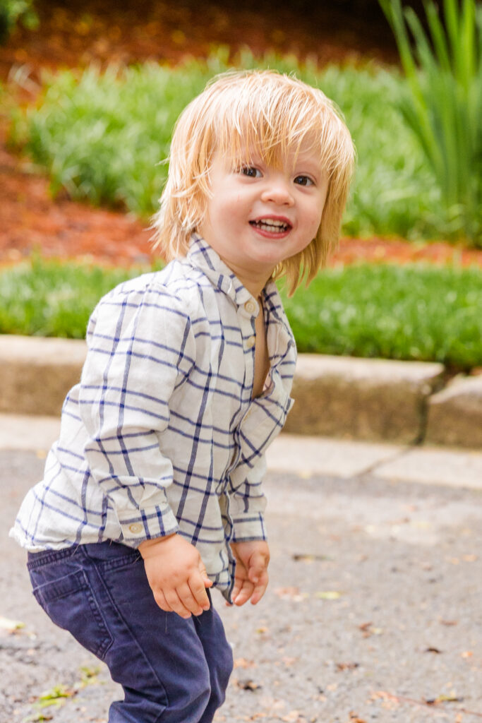 Toddler boy jumping and laughing in coordinated blue and white outfit.