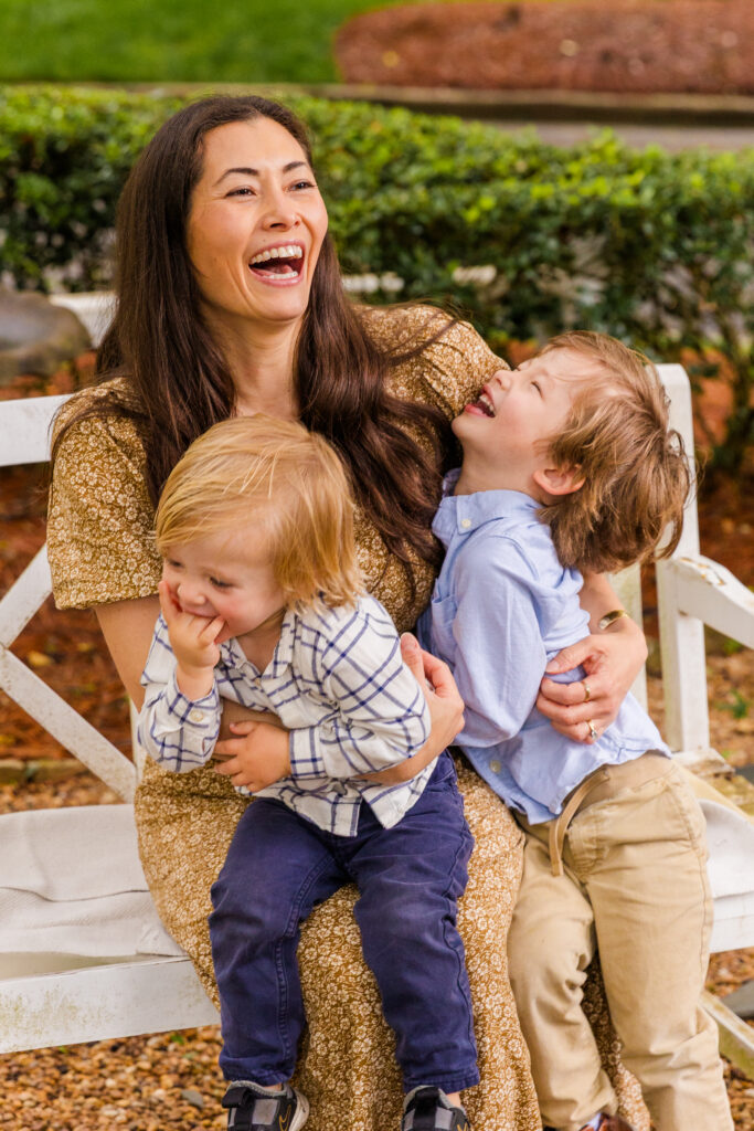 Joyful moment of a mother laughing with her two sons on a white bench.