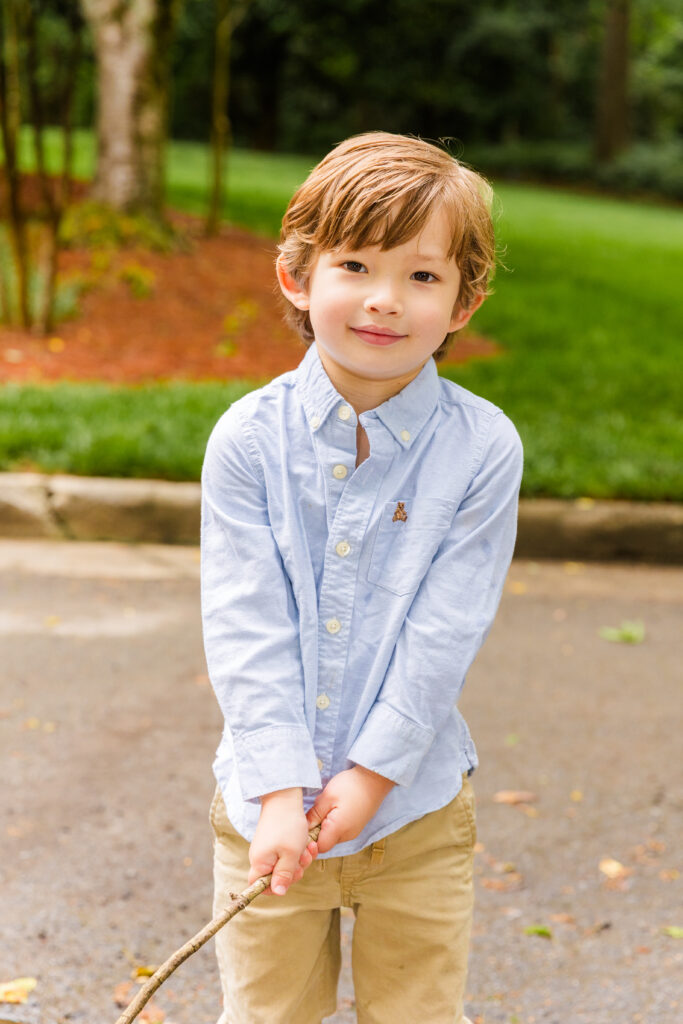 Boy in blue shirt and beige pants standing on path holding a stick.