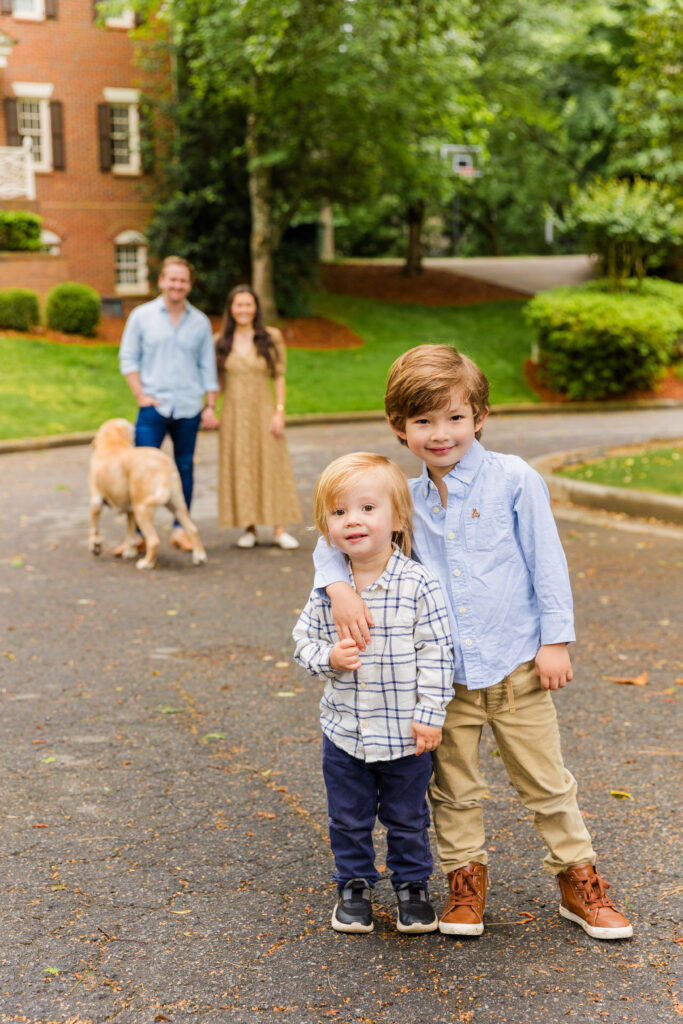 Two brothers hug while their parents and dog appear blurred in the background.