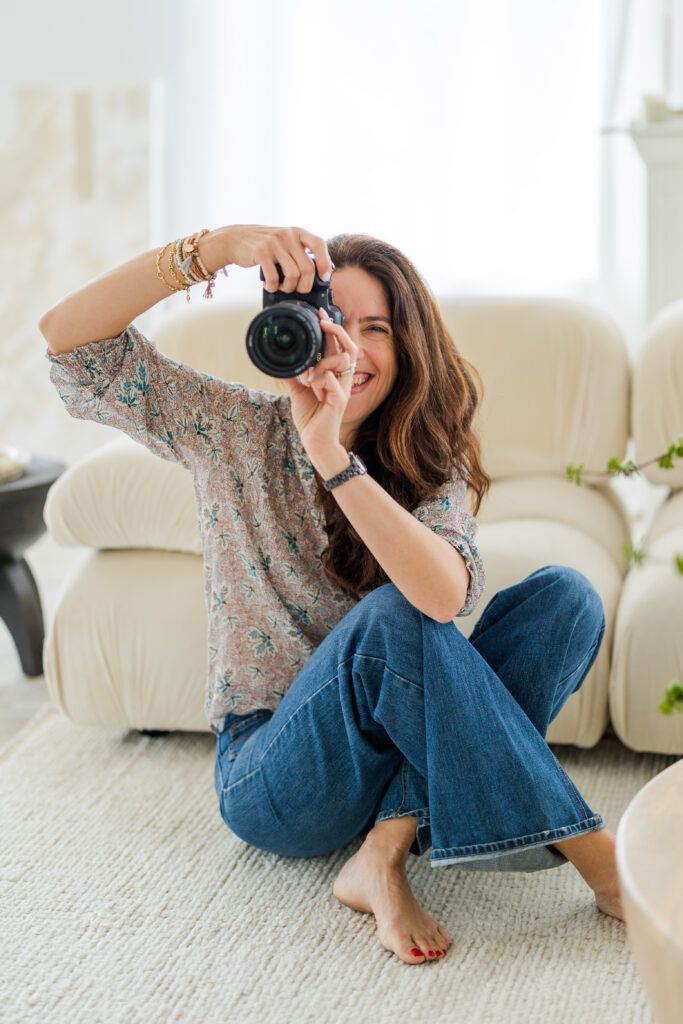 woman wearing blue jeans sitting on the floor in front of a sofa smiling at the camera through a photo lens