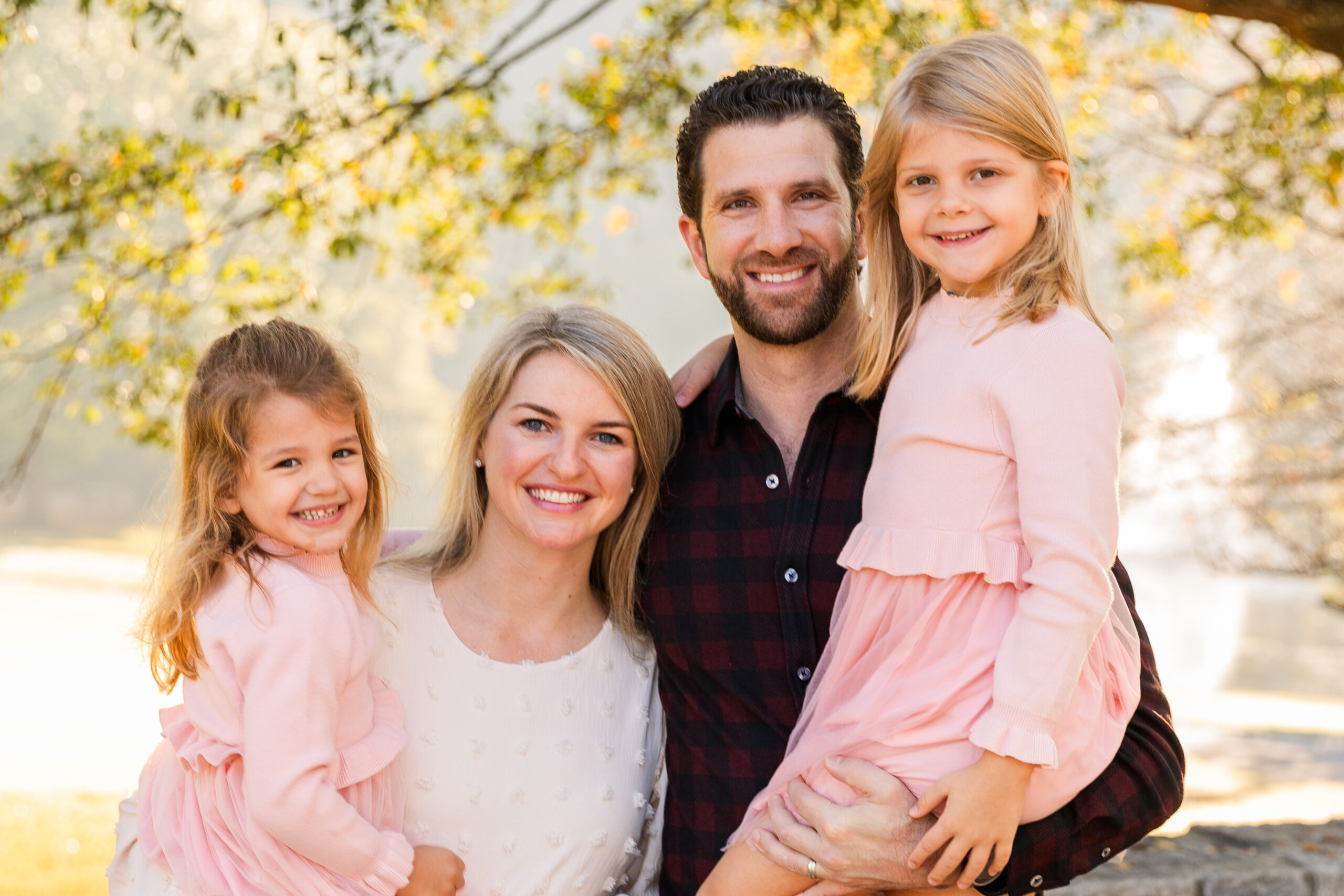 Close up of Parents each holding one of their daughters in light pink dresses while sharing a family hug in an Atlanta park during a family photo session with Laure Photography.
