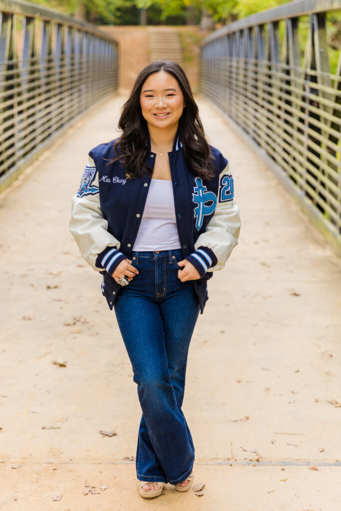 Pace Academy senior Mia standing on a bridge in Brookhaven wearing jeans, white top, and leather jacket, hands in pockets.
