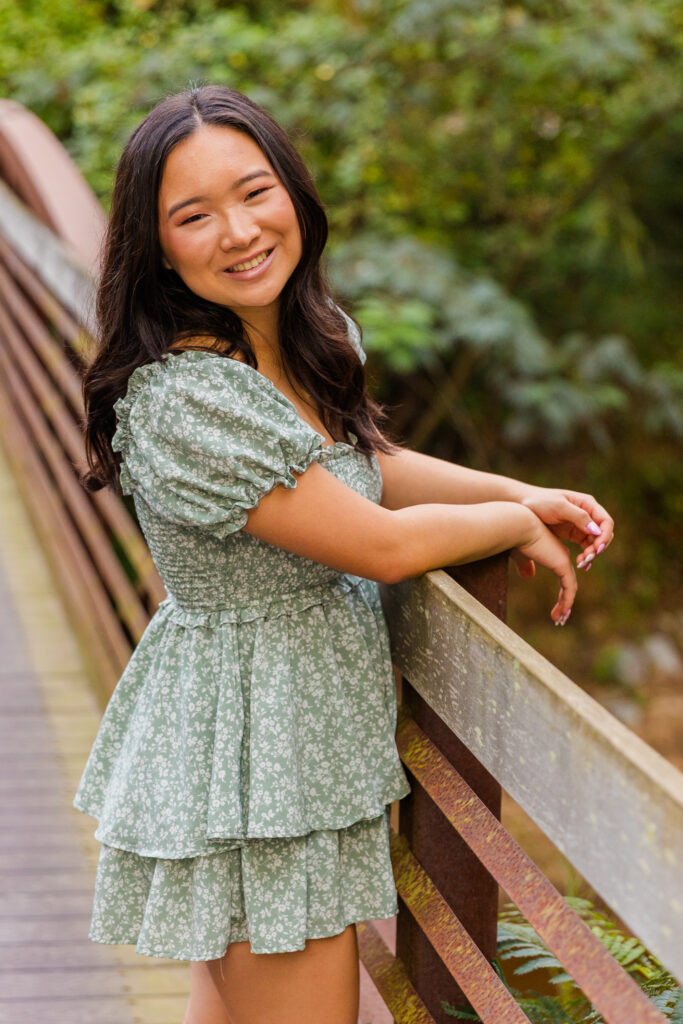 Pace Academy senior looking over shoulder on park bridge wearing green and white floral dress.