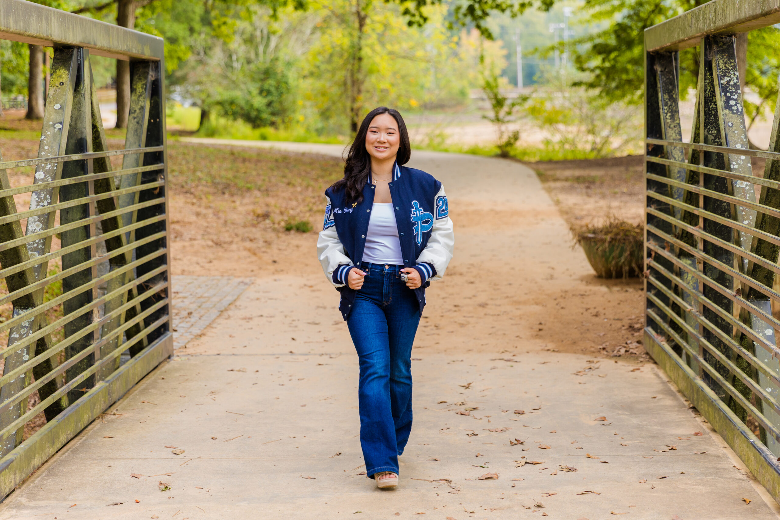 Full-body photo of Pace Academy senior walking on a park bridge in Brookhaven with trees in the background.