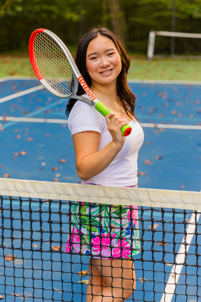 Pace Academy senior posing behind tennis net with racket on shoulder during Brookhaven session.