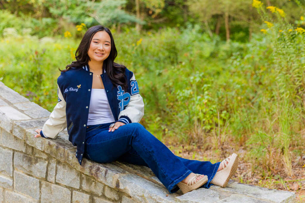 Pace Academy senior Mia sitting on a park wall wearing jeans, white top, and leather jacket.