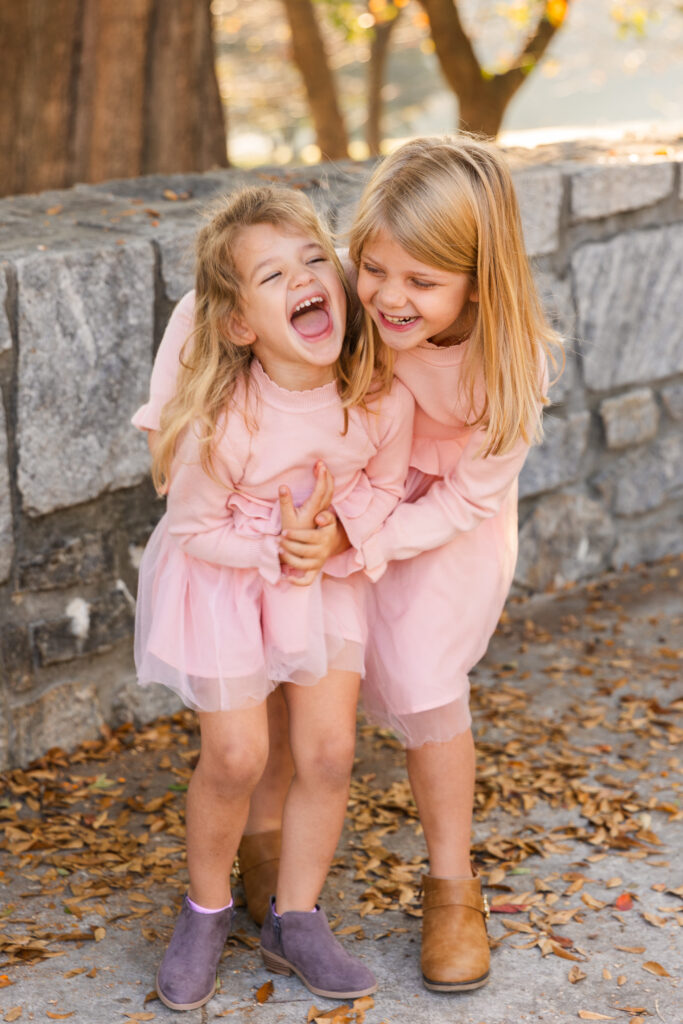 Two young sisters in light pink dresses playing together during a family photo session in an Atlanta park with Laure Photography.