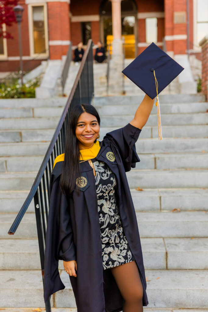 Close-up of Pallovi holding her graduation cap in the air with Georgia Tech buildings in the background
