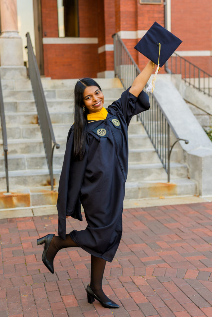 Fun graduation photo of Pallovi holding her cap in the air while posing on Georgia Tech campus