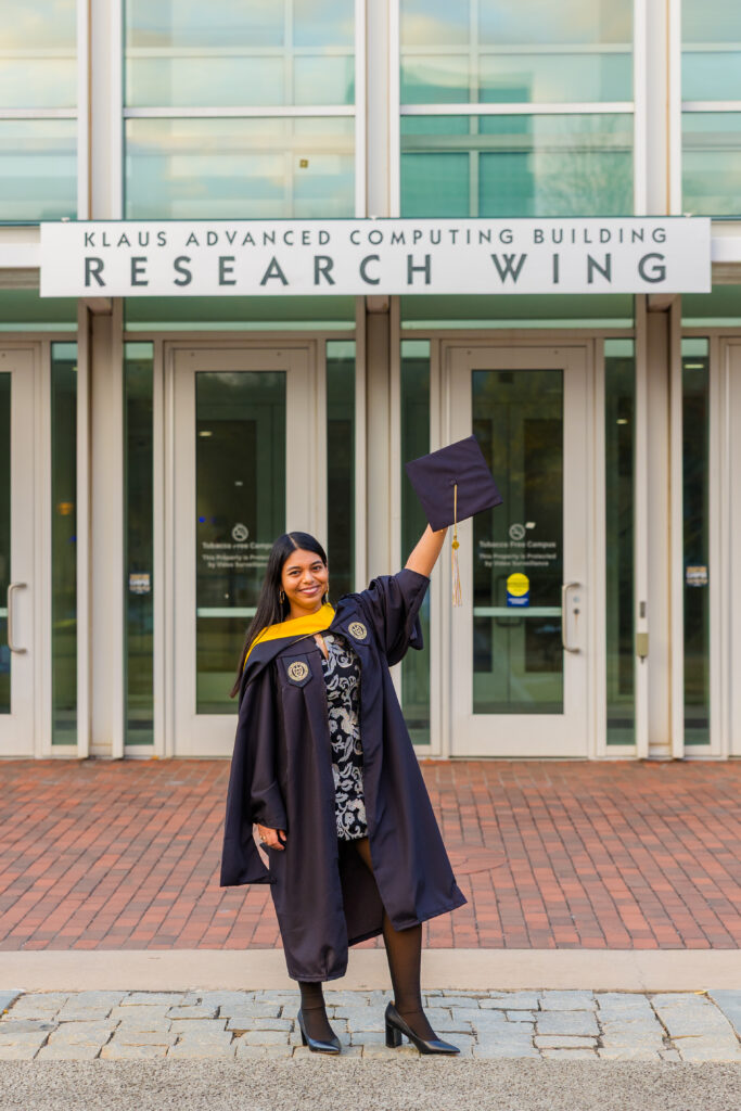 Pallovi holding her graduation cap high in front of the Kaus Advanced Computing building at Georgia Tech