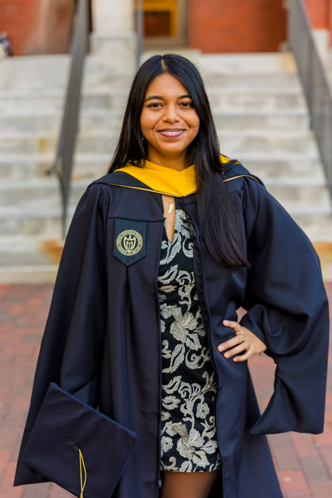 Three-quarter body graduation portrait of Pallovi standing on Georgia Tech campus holding her cap
