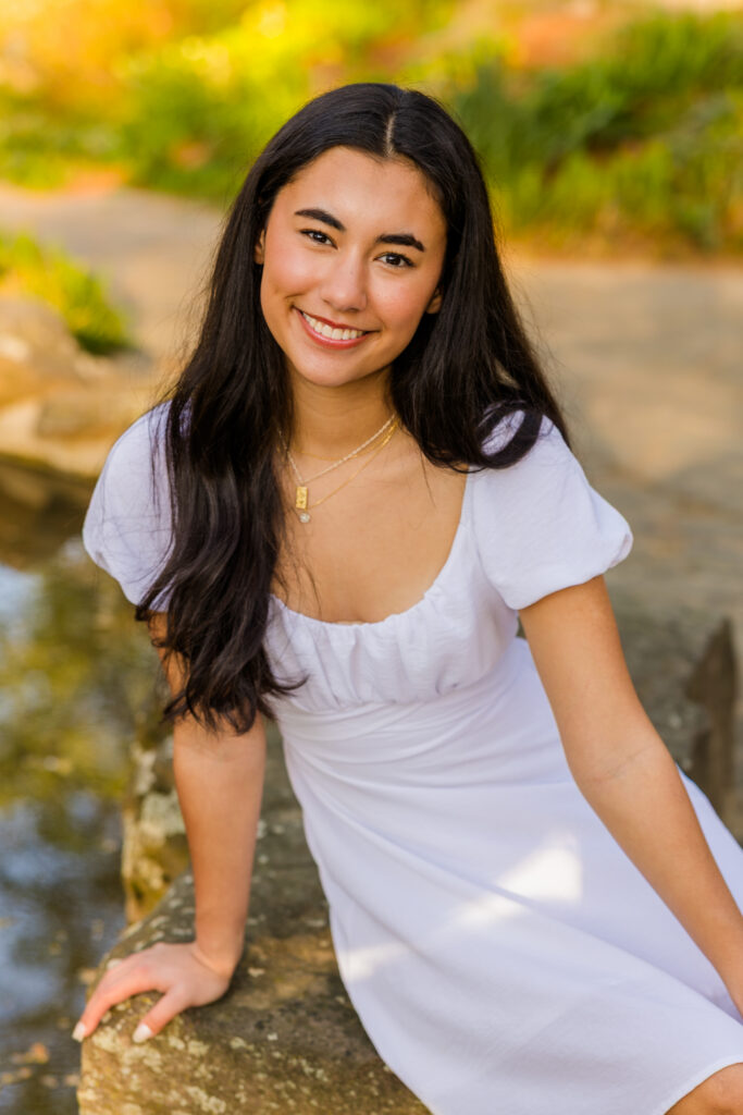 Senior sitting on rocks by pond in Atlanta park wearing white dress