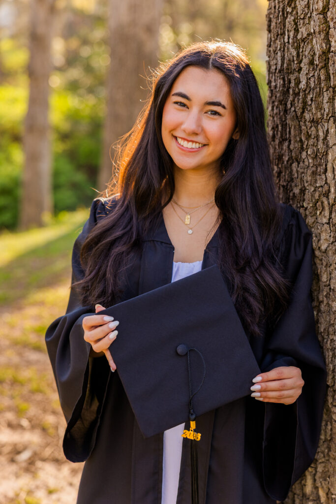 Atlanta senior standing by tree holding graduation cap and wearing gown