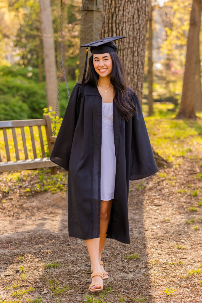 Senior walking in Atlanta park wearing white dress and graduation gown