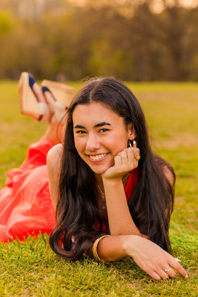 Close-up of Atlanta senior in orange dress laying on her stomach resting head on hand