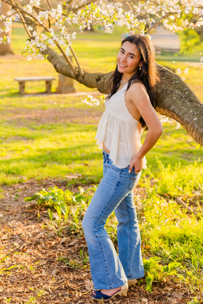 Wide shot of senior leaning against blooming tree in Piedmont Park