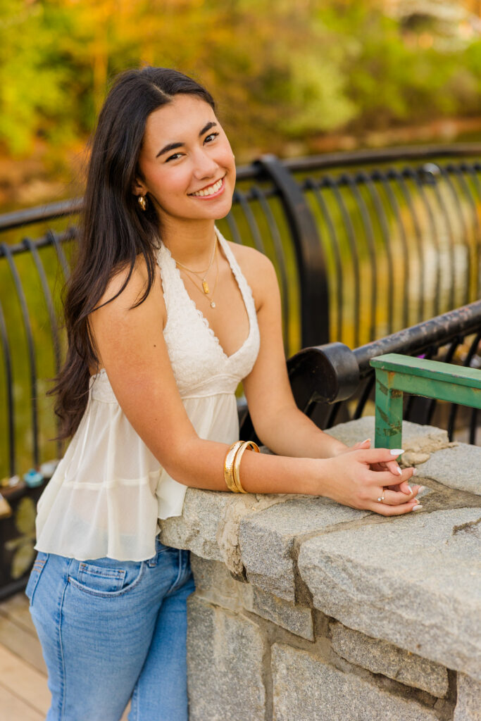 Senior leaning on bridge in Atlanta park wearing jeans and white sleeveless top