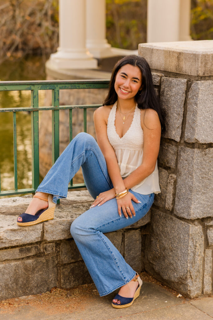Senior sitting on bridge pole with one leg up wearing jeans and white top